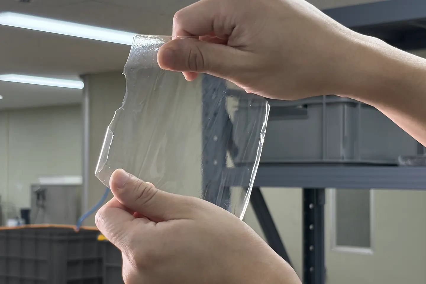 Two hands holding up a clear polymer membrane sample